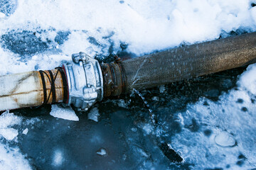 Winter. Everything is covered with snow. Leak in the connection of pipes pumping water out of the...