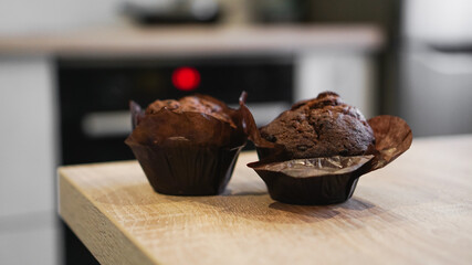 Two chocolate muffins on a wooden table against the background of a modern kitchen
