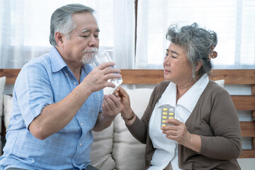 Asian elderly couple, Taking care of health in retirement, Senior woman helping her husband take a pills or vitamin pills at home.
