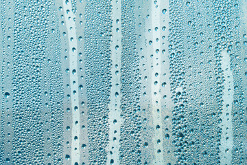 Abstract background ornament with blue water drops.Raindrops are blue in color.Sparkling shiny water surface on the glass.Water drops in the form of balls or spheres.Colored raindrops backdrop