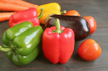Red and green bell peppers with other colorful vegetables on dark brown wooden background