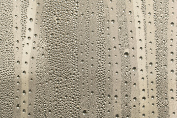 Raindrops on the glass in rainy weather.The glittering, shiny surface of water on glass.Water drops in the form of balls or spheres.Grey raindrops background. Abstract backgrounds ornament with water