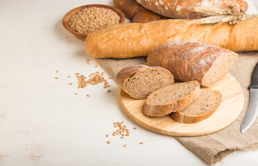 Sliced bread with different kinds of fresh baked bread on a white wooden background. side view, copy space.