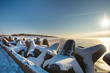 Curonian spit pier with protecting barrier rocks, dunes and an empty beach covered by snow. Beautiful sunny weather and blue sky. Klaipeda Lithuania