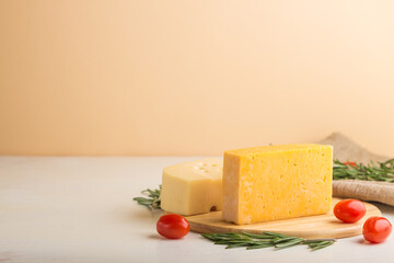 Various types of cheese with rosemary and tomatoes on wooden board on a white and orange background. Side view, copy space.
