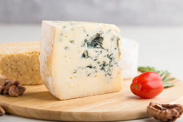 Blue cheese and various types of cheese with rosemary and tomatoes on wooden board on a white background . Side view, selective focus.