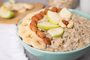 Bowl of delicious oatmeal with fruits and nuts on table, closeup