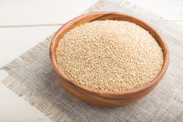 Wooden bowl with raw white quinoa seeds on a white wooden background. Side view, close up.
