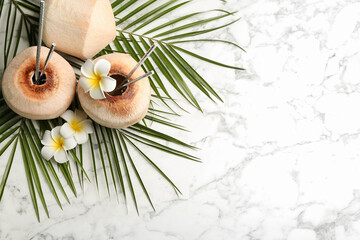 Fresh coconut with drinking straws and flowers on white marble table, flat lay. Space for text