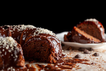 Angled side view of a gourmet round chocolate cake with coconut shreds on icing. Two slices were removed and placed on white porcelain plate with a metal fork for serving.  Chocolate chips on surface.