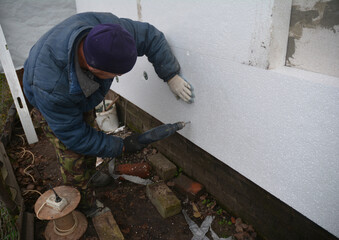 A man is insulating the house facade with polystyrene boards. Thermal insulation of an exterior house wall using expanded polystyrene.