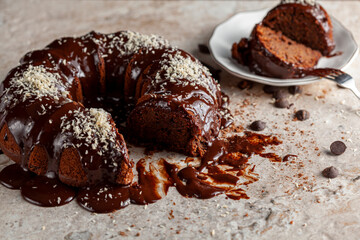 Angled side view of a gourmet round chocolate cake with coconut shreds on icing. Two slices were removed and placed on white porcelain plate with a metal fork for serving.  Chocolate chips on surface.