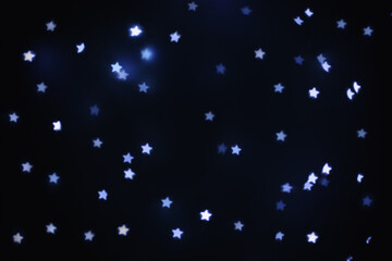 Beautiful star shaped lights on black background, space for text