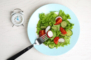 Alarm clock and plate with salad on white wooden