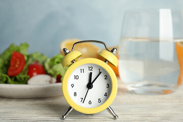 Fototapeta na wymiar Alarm clock and healthy food on white wooden table. Meal timing concept