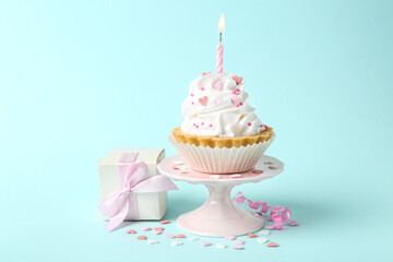 Delicious cupcake with candle and gift box on turquoise background