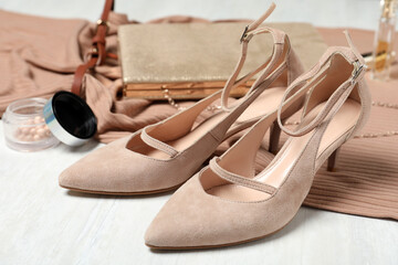 Beige suede shoes, cosmetics and accessories on white wooden table