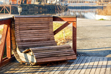 Outdoor furniture, a wooden chair on the river bank is illuminated by the rays of the bright sun against the background of the calm smooth surface of the water in blur.