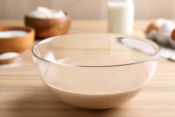 Glass bowl with batter on wooden table in kitchen, closeup