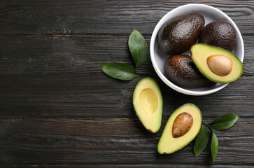 Whole and cut avocados on dark wooden table, flat lay. space for text