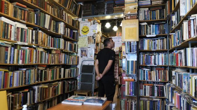 Customer in cozy secondhand bookshop looking at the books, bookstore interior