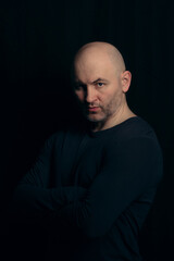 Portrait of a brutal bald man in a dark style on a black background. A bald athletic guy in a black...