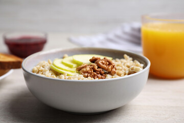 Tasty oatmeal porridge with walnuts and apple slices on white wooden table, closeup