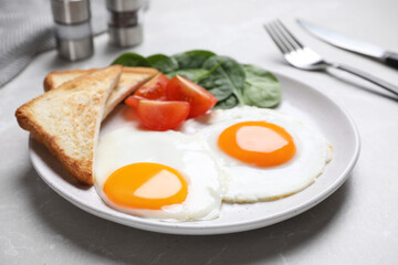 Tasty breakfast with fried eggs, toasts and spinach served on light grey table, closeup