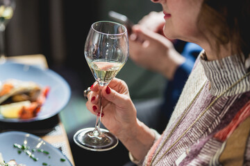 woman holds glass of white wine. people consider the color of the wine and try how it smells in different glasses