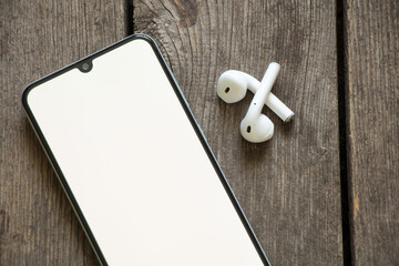 phone with white screen wireless headphones on wooden table