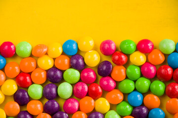 Fototapeta na wymiar Skittles candy on the yellow table, colorful sweet candy background
