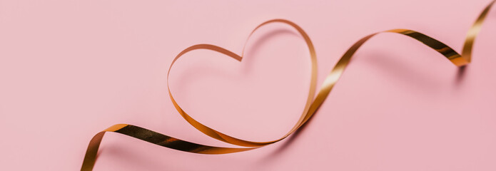 shape heart by gold ribbon on isolated pink background