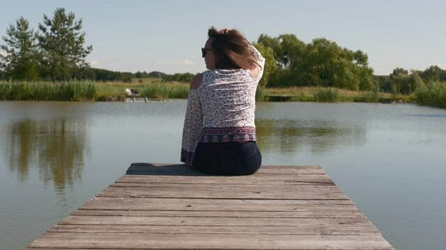 Back view of young woman sitting and relaxing on the pond in summer. Summertime.