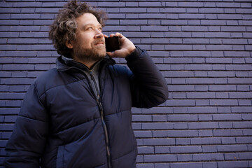 horizontal pic of Caucasian man with long hair and beard talking on his cell phone on a blue brick wall