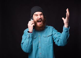 Photo of angry bearded man talking on phone over dark background.