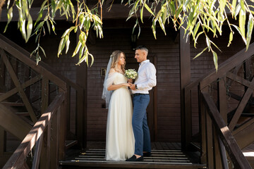 Beautiful bride and groom near a wooden stylish house. Sunny day.