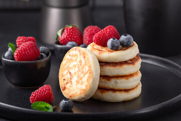 Stack of cottage cheese pancakes with fresh berries on dark ceramic plate. Syrniki - Image