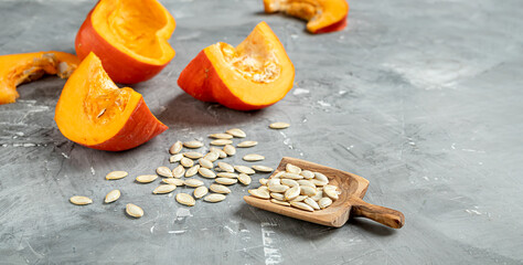 Slices of fresh autumn pumkins and pumkin seeds in a wooden spoon on a grey background with copy spce