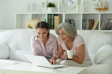 Obraz premium mother and daughter sitting at table with laptop, at home