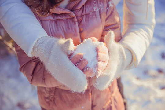 mom holds her daughter's hands in her fur gloves on the street in winter, snow.