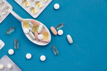 pills and vitamins in a ceramic spoon, other pills lie nearby