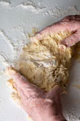 Top view of woman's hands kneading on white countertop with flour, selective focus, vertical
