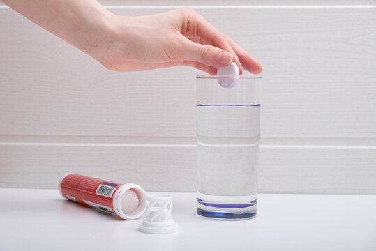 female hand puts a pill in a glass of water