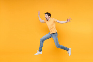 Full length side view of young overjoyed hurrying excited fun surprised man 20s in casual t-shirt jeans high jumping up looking aside spreading hands isolated on yellow background studio portrait.