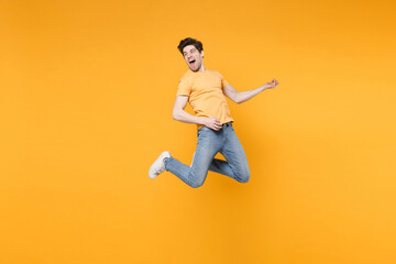 Fototapeta na wymiar Full length of young caucasian fun happy excited man 20s wearing casual basic t-shirt jeans high jumping up play guitar hand gesture expression isolated on yellow color background studio portrait