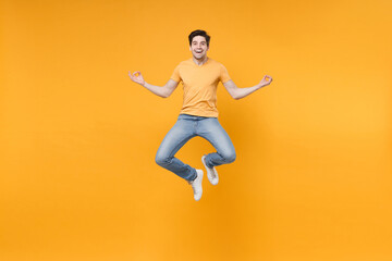 Fototapeta na wymiar Full length body of young meditating happy excited man 20s in casual t-shirt jeans high jump up levitating hold hands in yoga om gesture look camera isolated on yellow background studio portrait.