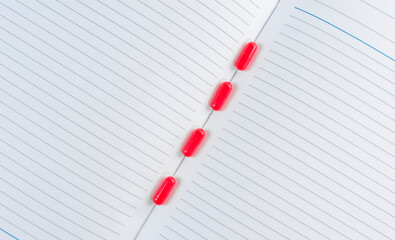 Red pills in an open notebook with. Concept of regularity and timing of pills.