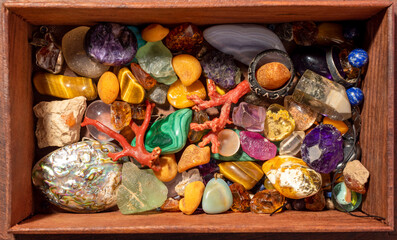 Gemstone collection in wooden chest, close-up. Mixed rough and tumbled stones, silver rings and pendants. Top view.