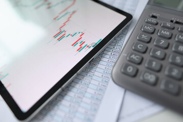 On table is tablet with commercial charts, calculator and documents with reports
