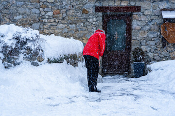 Man with snow shovel cleans sidewalks in winter near house. Winter time, snowfall. France Europe.